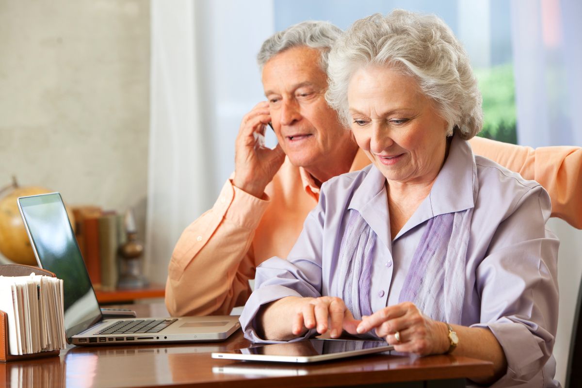Mulher de cabelos grisalhos usando notebook com expressão de conquista